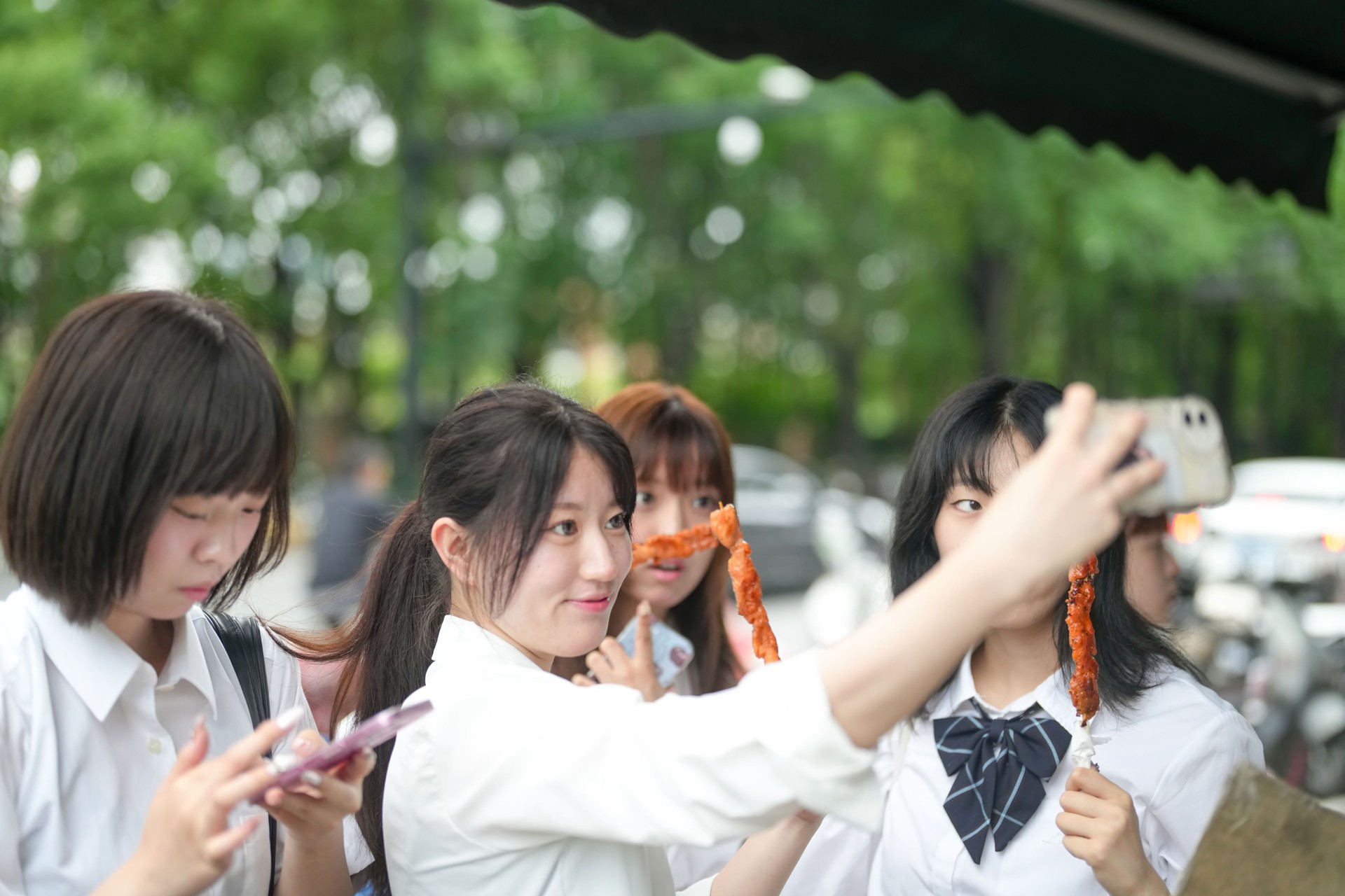 In early June in Pudong, Shanghai, seven Japanese high school girls in summer uniforms gather at a local street food stall, enjoying skewered meat and chatting before heading off to school together.
